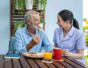 A senior man and a female caregiver eating together