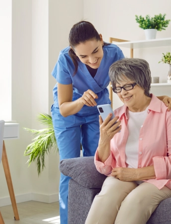 A senior woman holding a mobile phone and a female caregiver assisting her