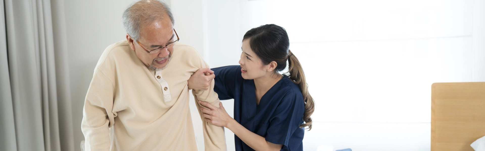 A female caregiver assisting a senior man to stand