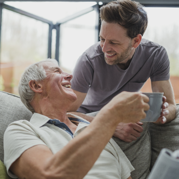 A male giving a cup of coffee to a senior man 