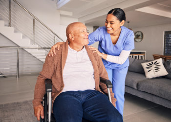 A senior man sitting on a wheelchair and a female caregiver looking at each other