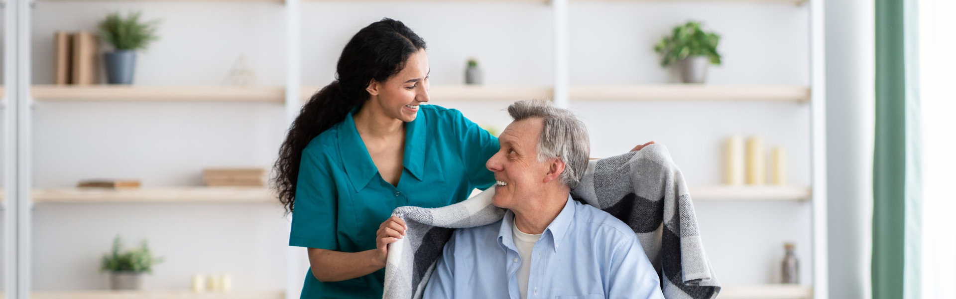 A female caregiver giving coat to a senior man sitting on a wheelchair